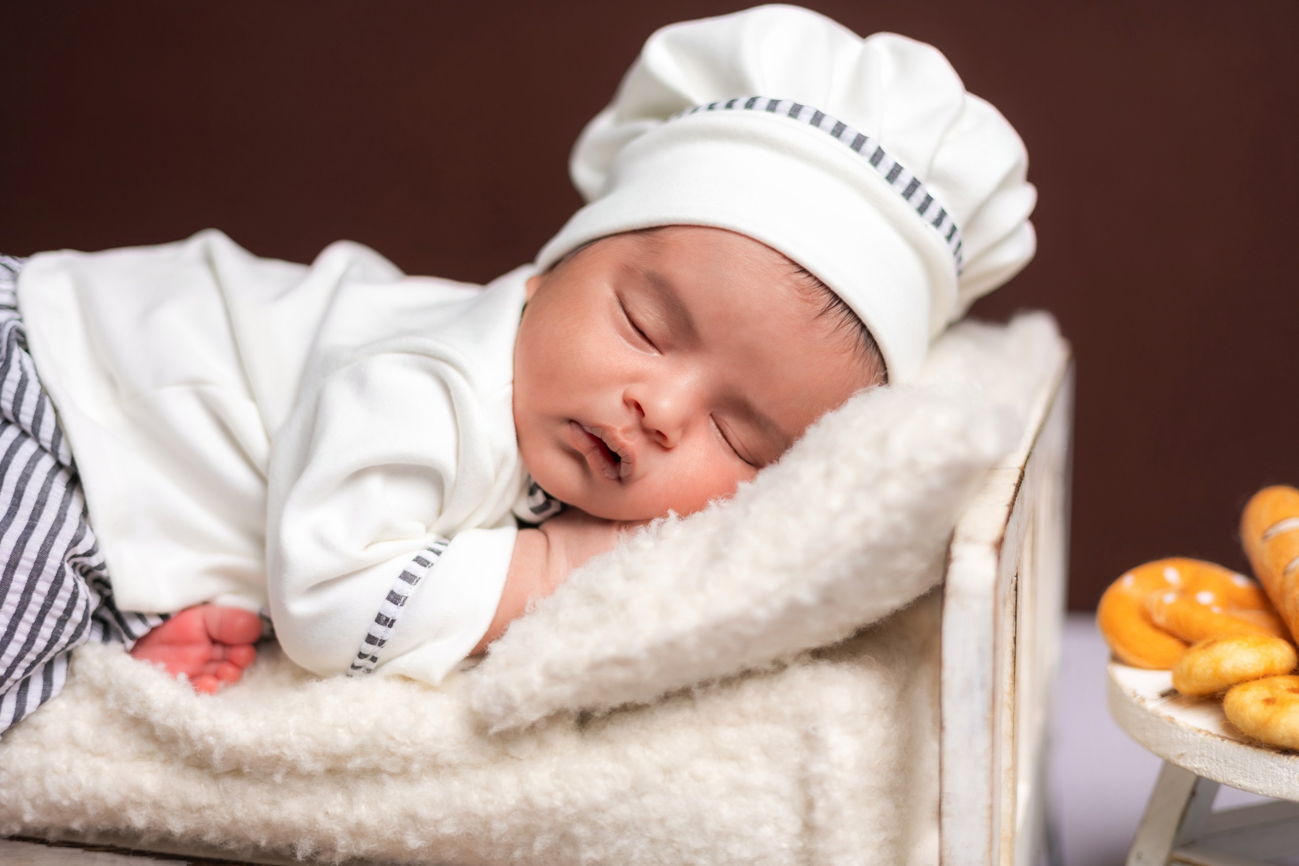 Sleeping newborn in a chef hat beside tiny oranges