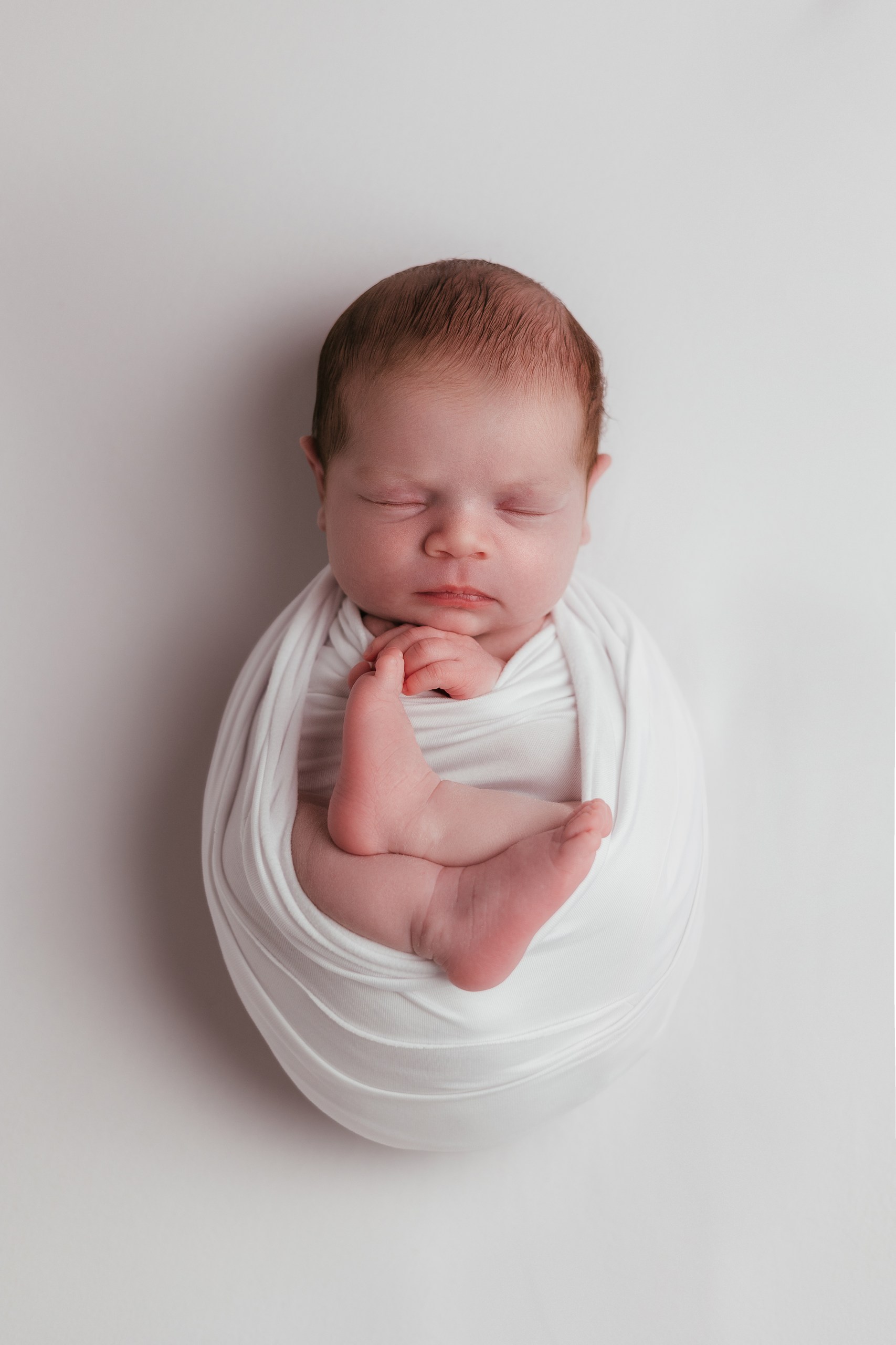 Sleeping newborn wrapped in white on a soft neutral backdrop