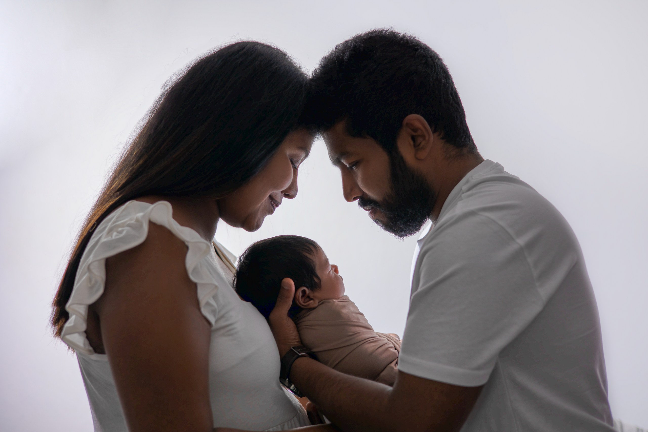 Parents gently leaning together over their newborn baby
