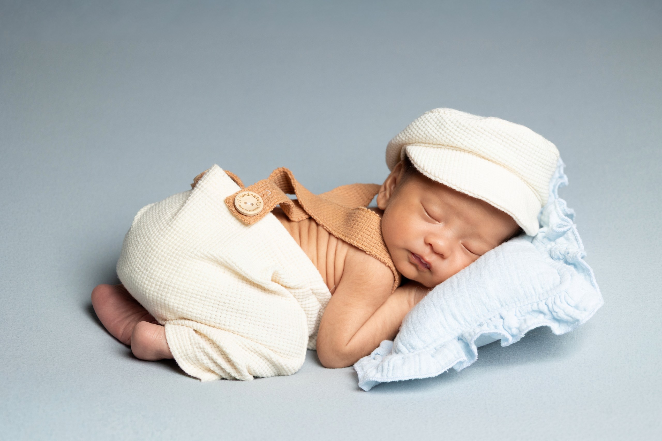 Newborn resting on pale blue cushions in a cream outfit