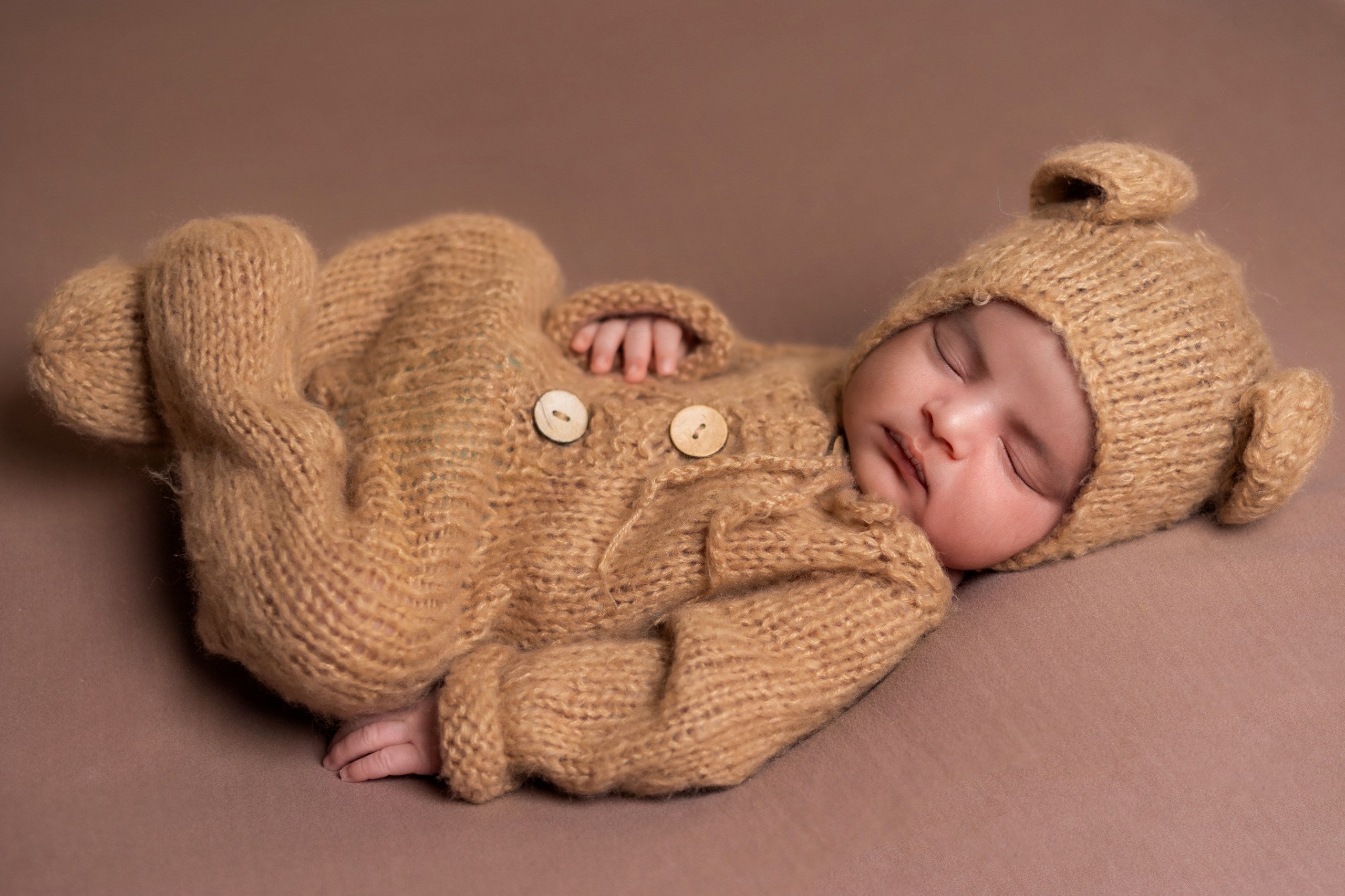 Sleeping baby in a knitted teddy-bear outfit