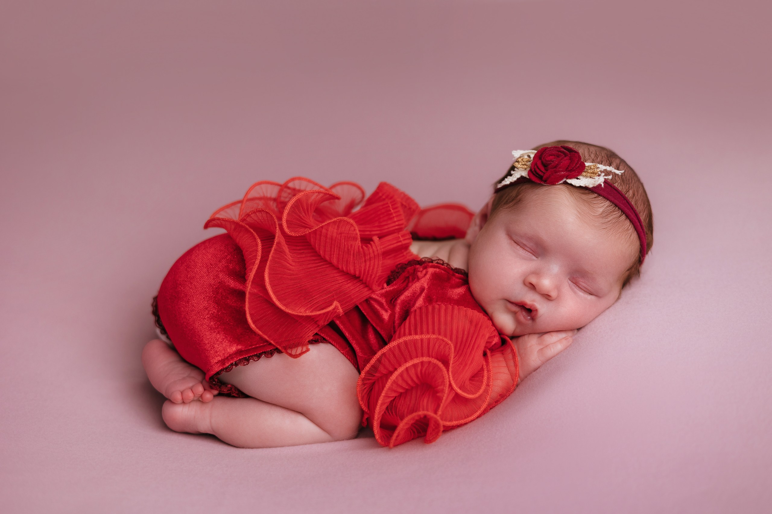 Newborn wearing a bright red outfit and floral headband