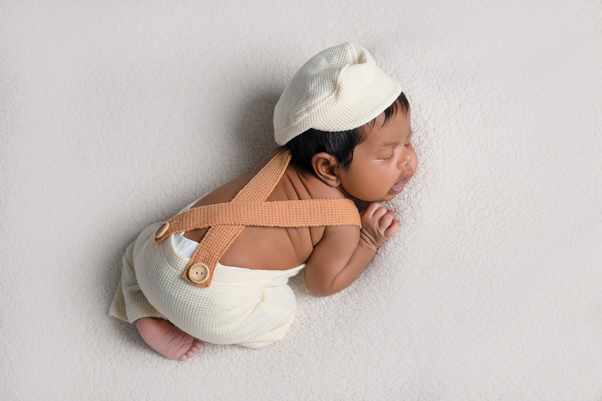Newborn in a cream bonnet resting in a parent's hands