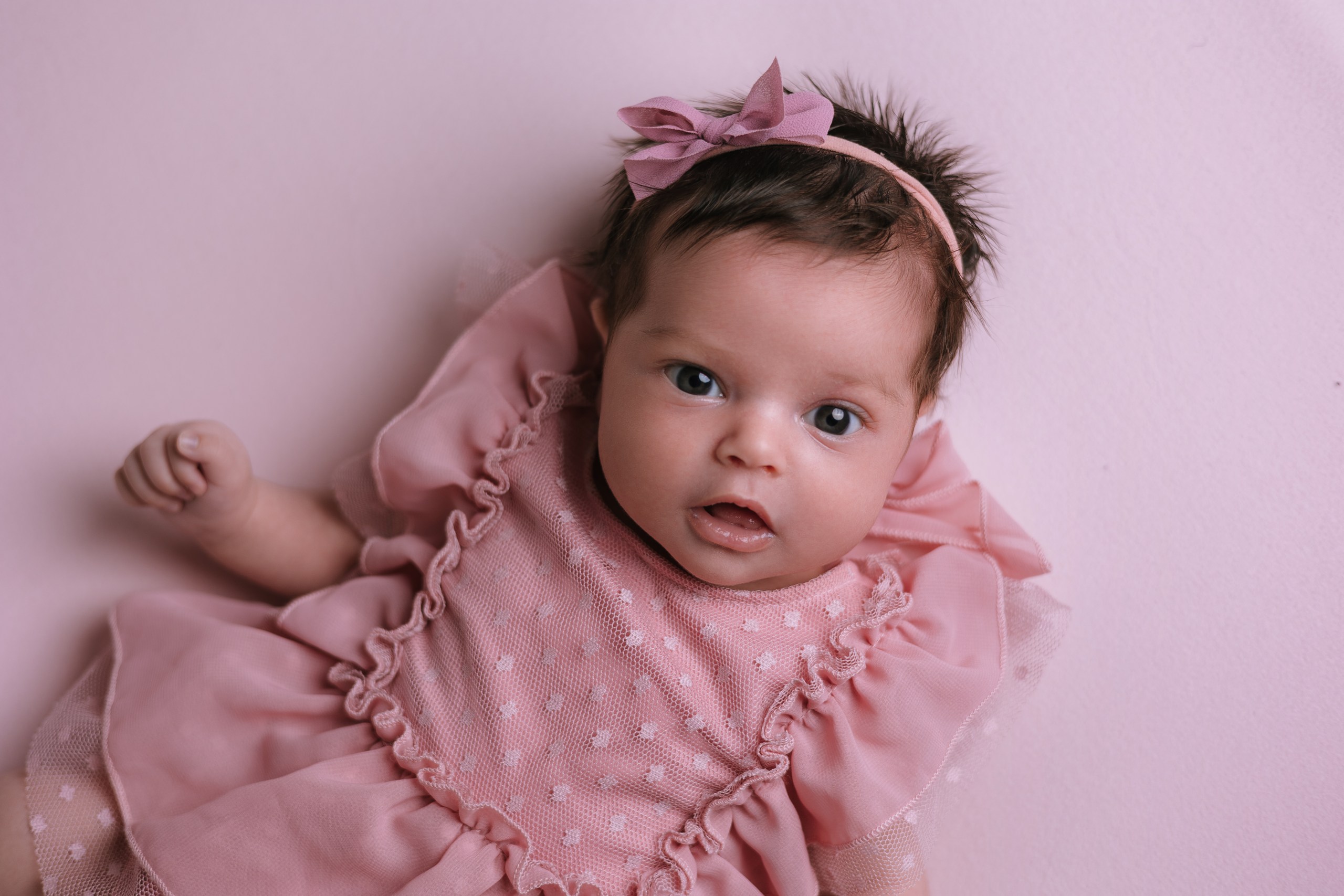 Awake baby with a floral headband on a pink backdrop