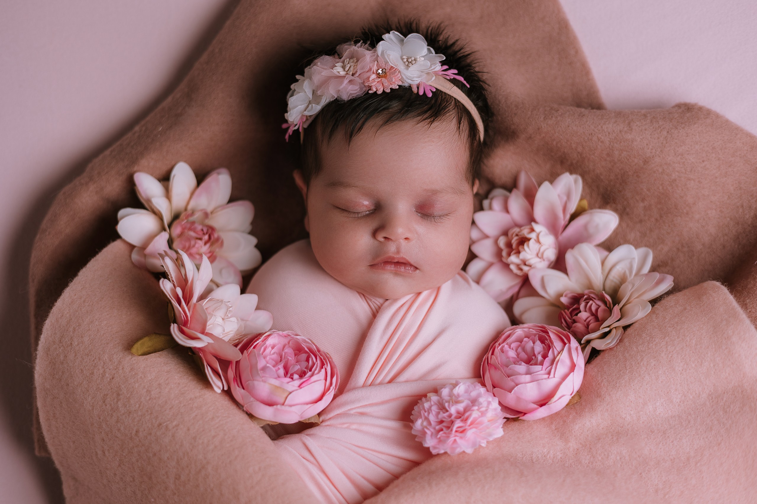 Baby in a pink wrap cradled in a parent's hands
