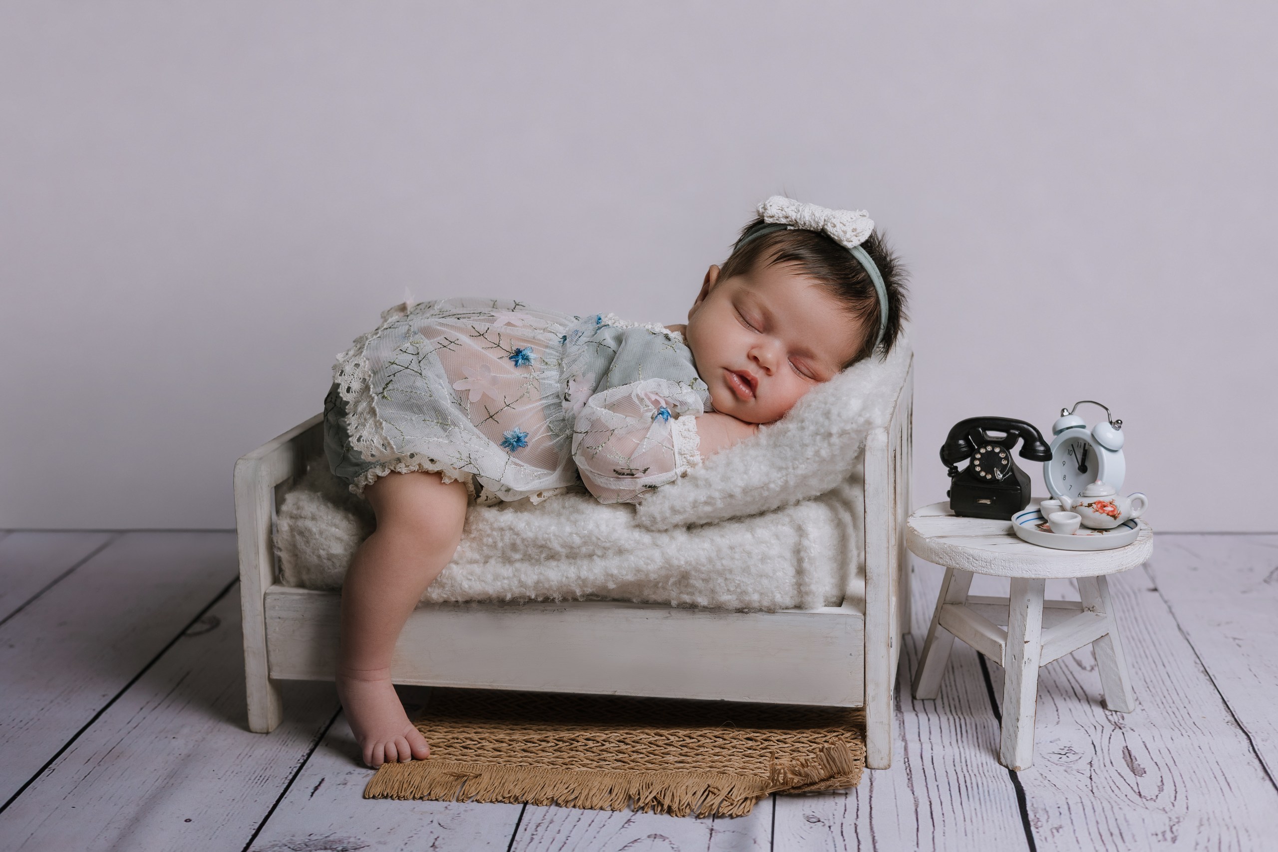 Baby resting on a miniature sofa in a soft grey outfit
